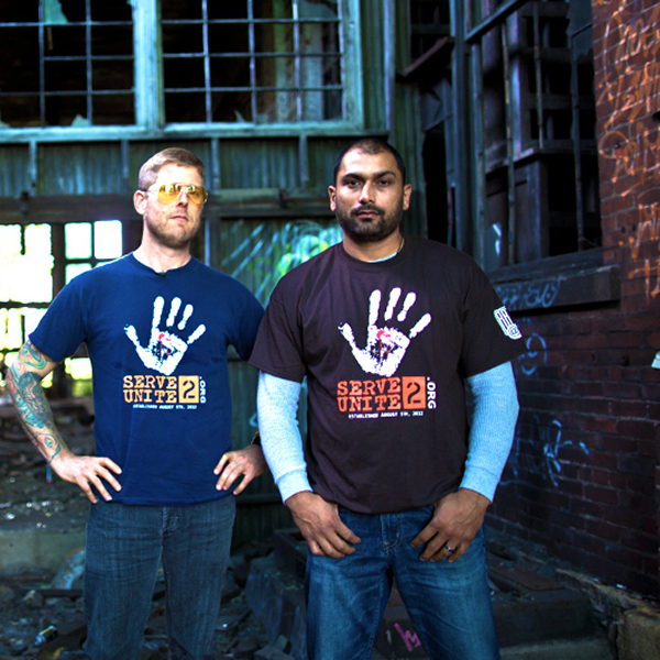 Two men stand side by side in front of a run down city building